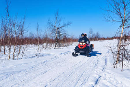 Russia, Perm Krai - March 28, 2021: people ride a snowmobile on a winter road among a birch forest-tundraのeditorial素材