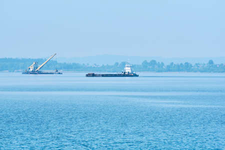 foggy river water landscape with cargo barge and grab dredge in the backgroundの写真素材