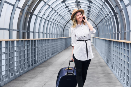 woman tourist with a suitcase smiling walks along the covered walkway gallery, speaks by phoneの写真素材