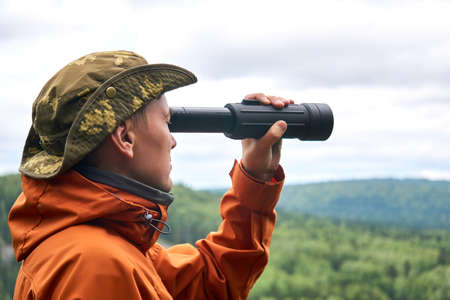 male traveler looks into the distance in a spotting scope against the natural landscapeの写真素材