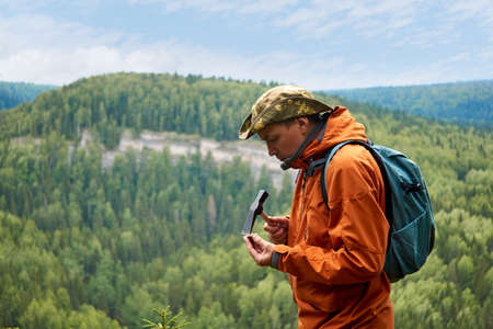 man geologist on an expedition examines a stone for hardness with a hammerの写真素材