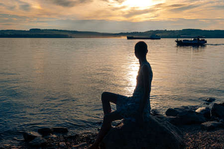 girl teenager with short hair sits on the banks of the river, looking at the shipsの写真素材