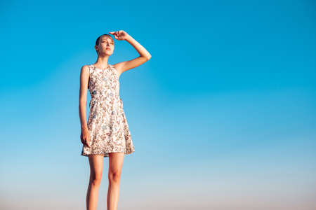 girl teenager in a dress with a short haircut standing looking into the distance against the background of the blue skyの写真素材