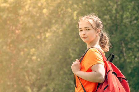 teenager girl in a bright orange t-shirt with backpack walks in nature