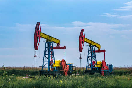 pumpjacks piston pumps operating at an oil well in field under cloudy skyの写真素材