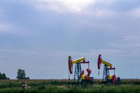 pumpjacks piston pumps operating at an oil well in field under cloudy sky