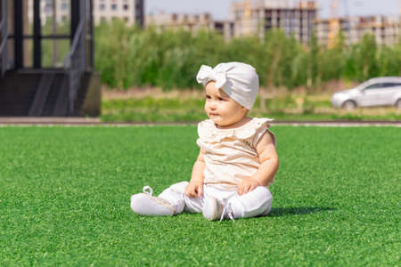 cute baby toddler sitting on a green lawn on the background of the city streetの写真素材