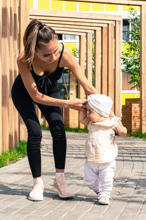 mother and toddler daughter walk in the city courtyard, child learns to walkの写真素材