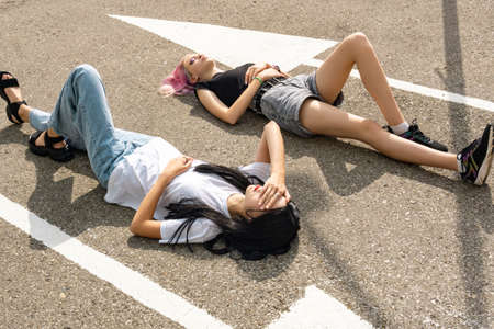 two teenager girls have fun lying on an empty road parallel to the markingsの写真素材