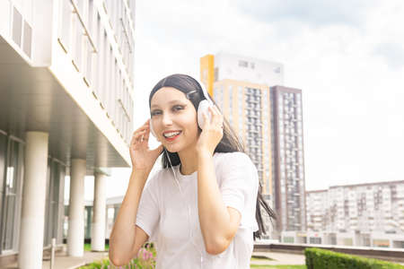 girl teenager listening to music with headphones outdoors on the background of the city