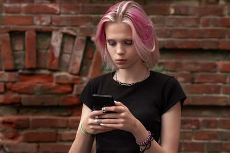 teenager girl communicates on the network using the phone against the background of an old wall