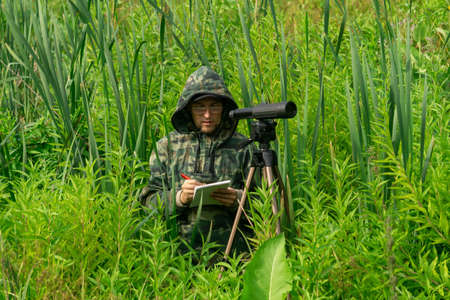 man ornithologist records the results of the observations while standing among the tall grass in the wetlandの写真素材