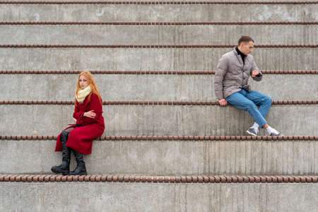 young couple in a quarrel, a guy and a girl are sitting looking in different directions in the empty standsの写真素材