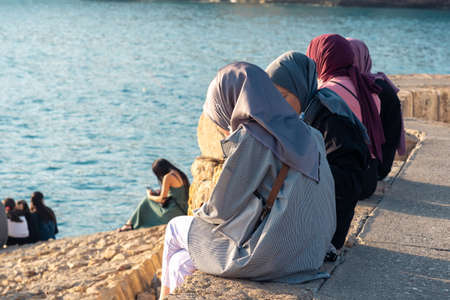 Antalya, Turkey - November 15, 2021: muslim girls sit on the mole on the seashore in the old harborのeditorial素材