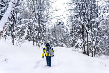 backpacker walks along a path in a snowy winter forest, following a quadcopter