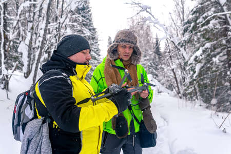 two men in the winter snowy forest launch a quadcopter