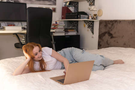 young woman lying with laptop on bed at home
