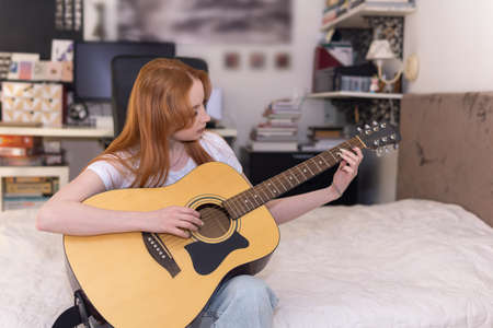 young woman playing acoustic guitar at home