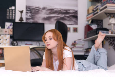 young woman lying with laptop on bed at home