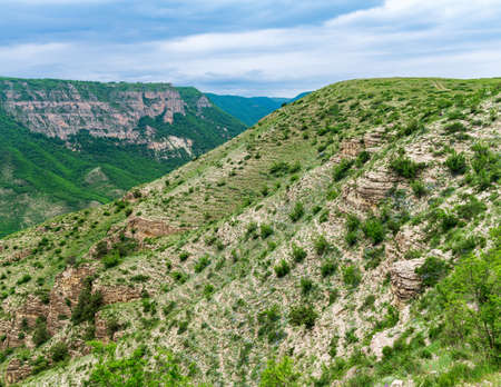 landscape with slopes of a mountain valley with weathered rocks and screes covered with shrubs