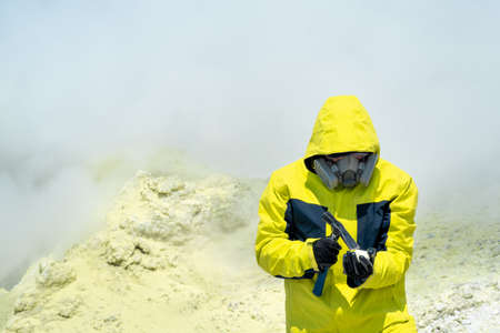 male volcanologist on the slope of a volcano among the vapors of a fumarole examines a sample of a mineralの写真素材