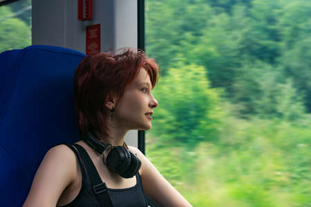 girl rides a train outside the city and looks out the window at a natural landscape blurred in motionの写真素材