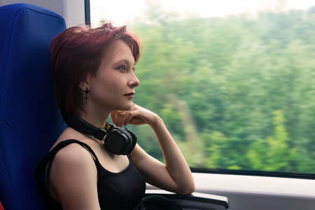 girl rides on a commuter train and looks out the window at a natural landscape blurred in motionの写真素材