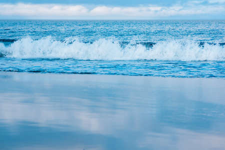 seascape, ocean surf on a smooth sandy beach, the sky is reflected in the wet sandの写真素材