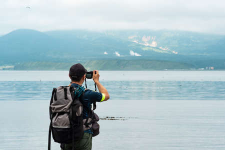 male tourist with a backpack photographs a foggy sea bay