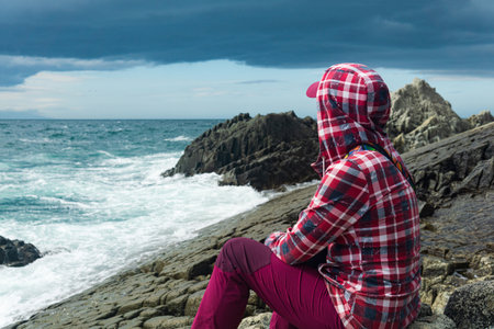 traveler sits on the shore of a stormy sea, on a natural pavement made of columnar graniteの写真素材