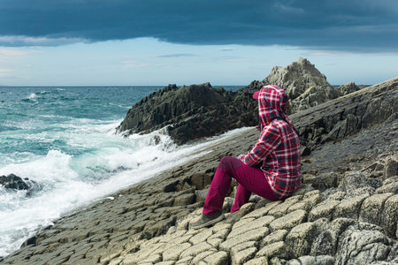 traveler sits on the shore of a stormy sea, on a natural pavement made of columnar graniteの写真素材