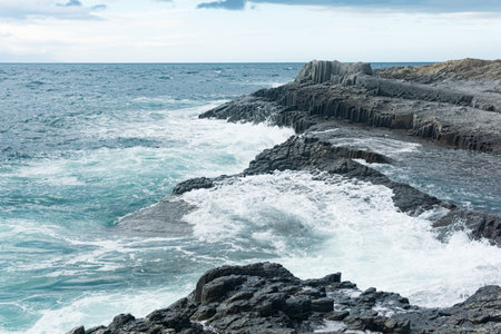 rocky seashore formed by columnar basalt against the stormy sea, coastal landscape of the Kuril...