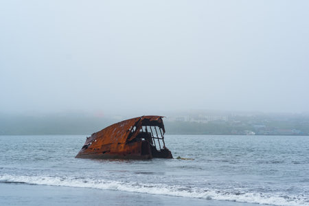 rusty shipwreck, remains of a ship washed ashore against a foggy seashoreの写真素材