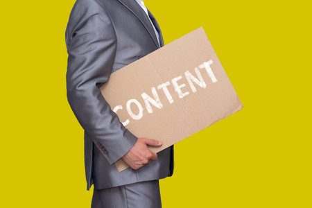 man in a suit carries a sheet of cardboard with the inscription "content", isolated on a yellow backgroundの写真素材