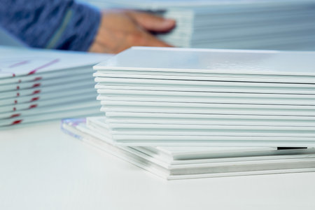 stack of freshly printed photobooks on the table close-up, blurry hands visible in the background