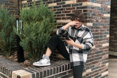 young man in cityscape sitting on curb with a phone making a facepalm