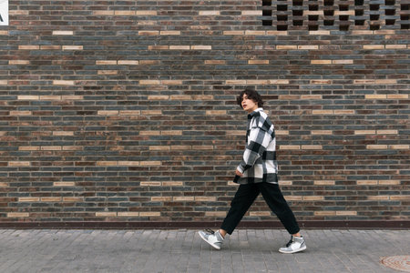 young man walks down the street in front of a brick wall