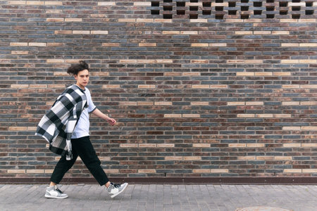young man walks down the street in front of a brick wallの写真素材