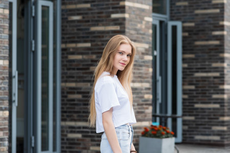 young woman stepped out of the door of a city building against a blurred urban backgroundの写真素材