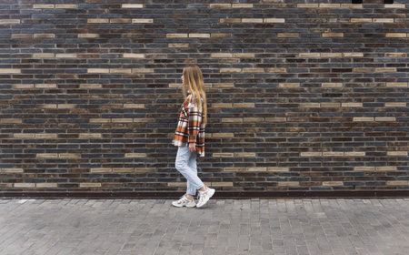 young woman walking down the street against a brick wallの写真素材