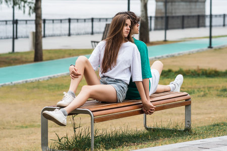 two young people, a guy and a girl, are sitting on a bench in a coastal parkの写真素材