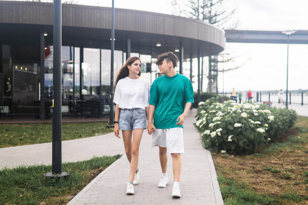two young people are walking and talking in a city coastal parkの写真素材