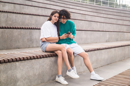 young couple together listening to the same music through headphones, sitting in empty standsの写真素材