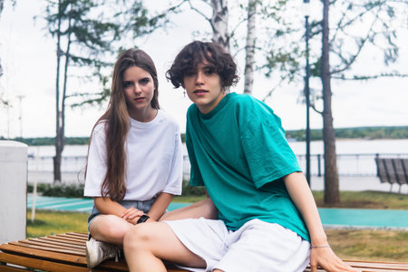two young people are sitting on a bench in a coastal parkの写真素材