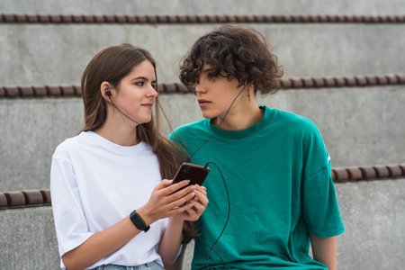 young couple together listening to the same music through headphones, sitting in empty standsの写真素材