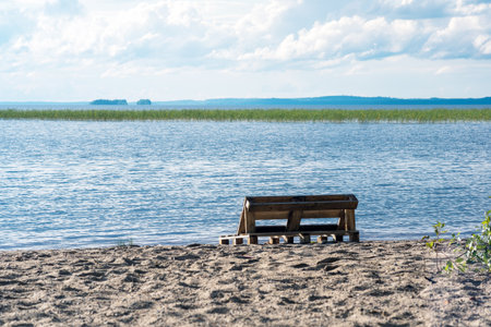bench made of old pallets on a sandy shore of a vast lakeの写真素材