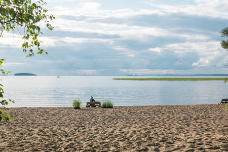 sandy beach on the shore of a lake, a woman traveler is sitting on a bench made of old vast palletsの写真素材