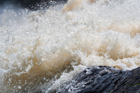 muddy turbulent stream under a rock during high water