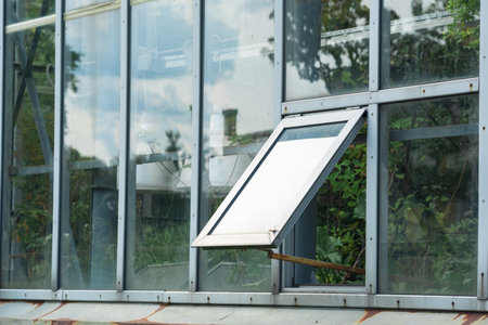 section of a glass wall of a tropical flower greenhouse with an open window, outside view