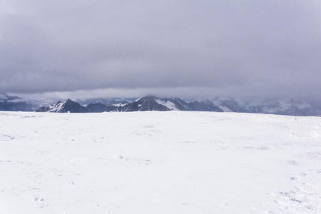 highland snowy plateau landscape, mountain range in clouds is visible on a distanceの写真素材